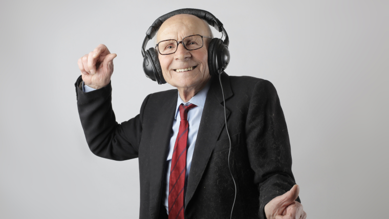 An old man wearing headphones listening to music and dancing.