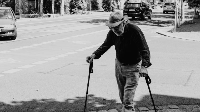 A black and white image of a man using two walking sticks.