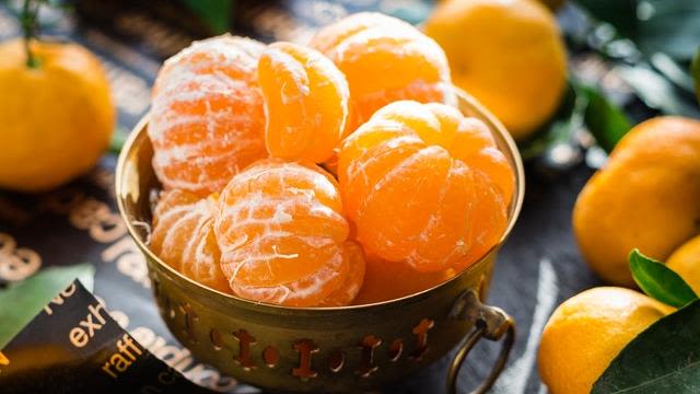 Bowl of peeled oranges with whole oranges scattered around.