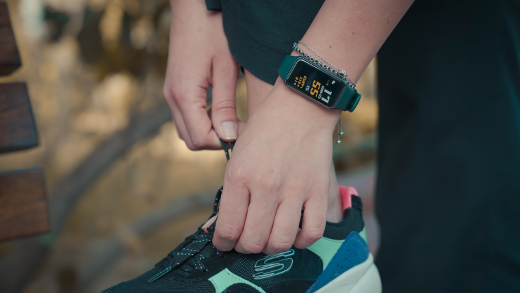 A woman who is wearing a wrist device to track her health while tying her running shoe.